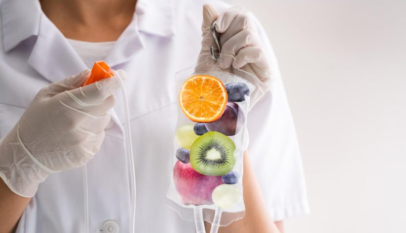 A healthcare professional holds an iv bag filled with various fruits like oranges, kiwis, and blueberries, symbolizing vitamin infusion.