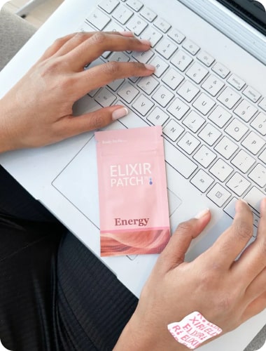 Person using a laptop with an "elixir patch energy" product and a patch applied on their hand visible.