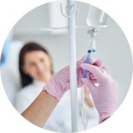 A healthcare professional adjusts an iv drip in a clinic, with a focus on her gloved hands and the iv stand.