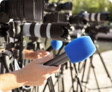 Row of cameras and microphones lined up outdoors, with a person adjusting one of the microphones.