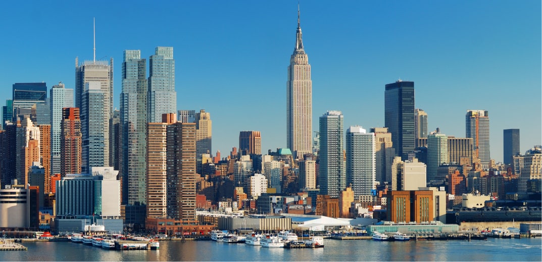 New york city skyline featuring the empire state building, with clear blue skies and boats docked along the waterfront.