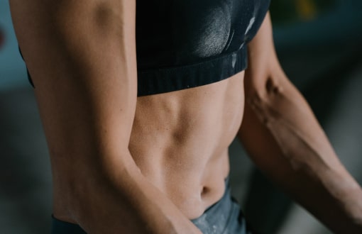 Close-up of a fit person's torso showing defined abdominal muscles, wearing a black sports bra and dark shorts.