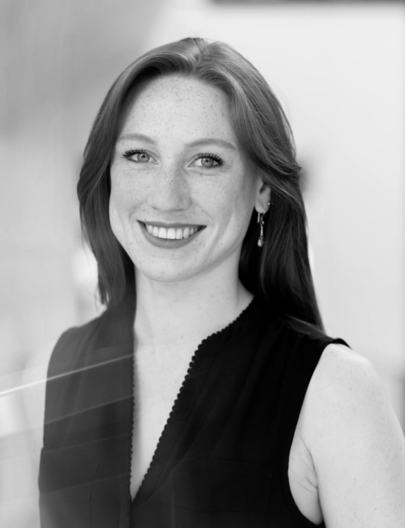 Black and white portrait of a smiling woman with long hair, wearing a sleeveless top and an earring.
