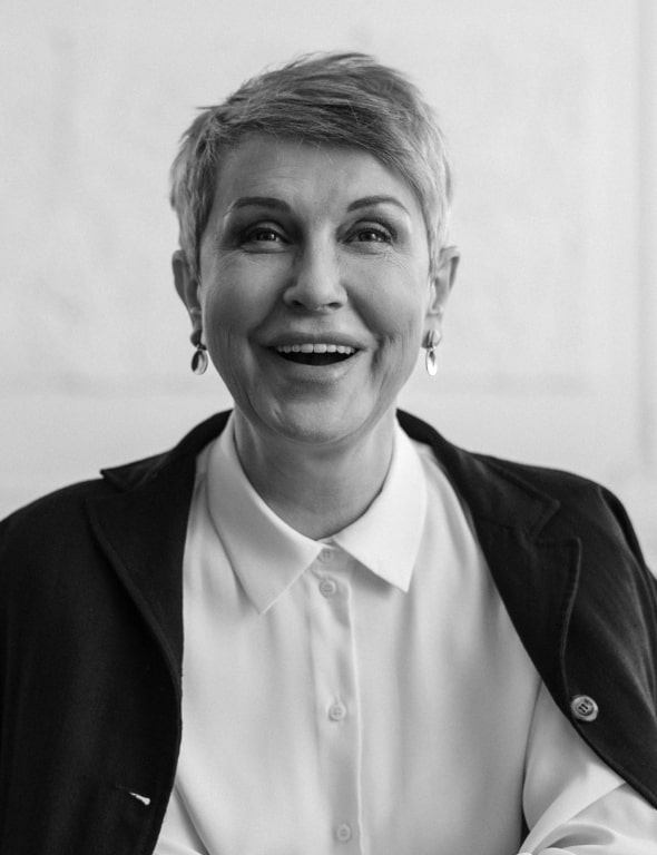 Black and white portrait of a smiling woman with short hair, wearing earrings and a white shirt under a dark blazer.