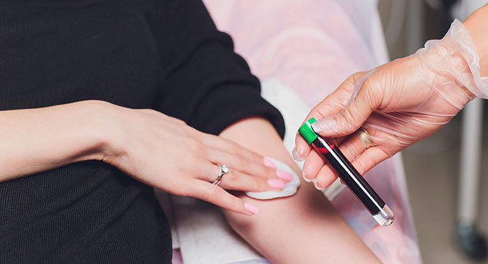 A healthcare professional wearing gloves applies a lancet device to a patient's finger to draw blood for testing.